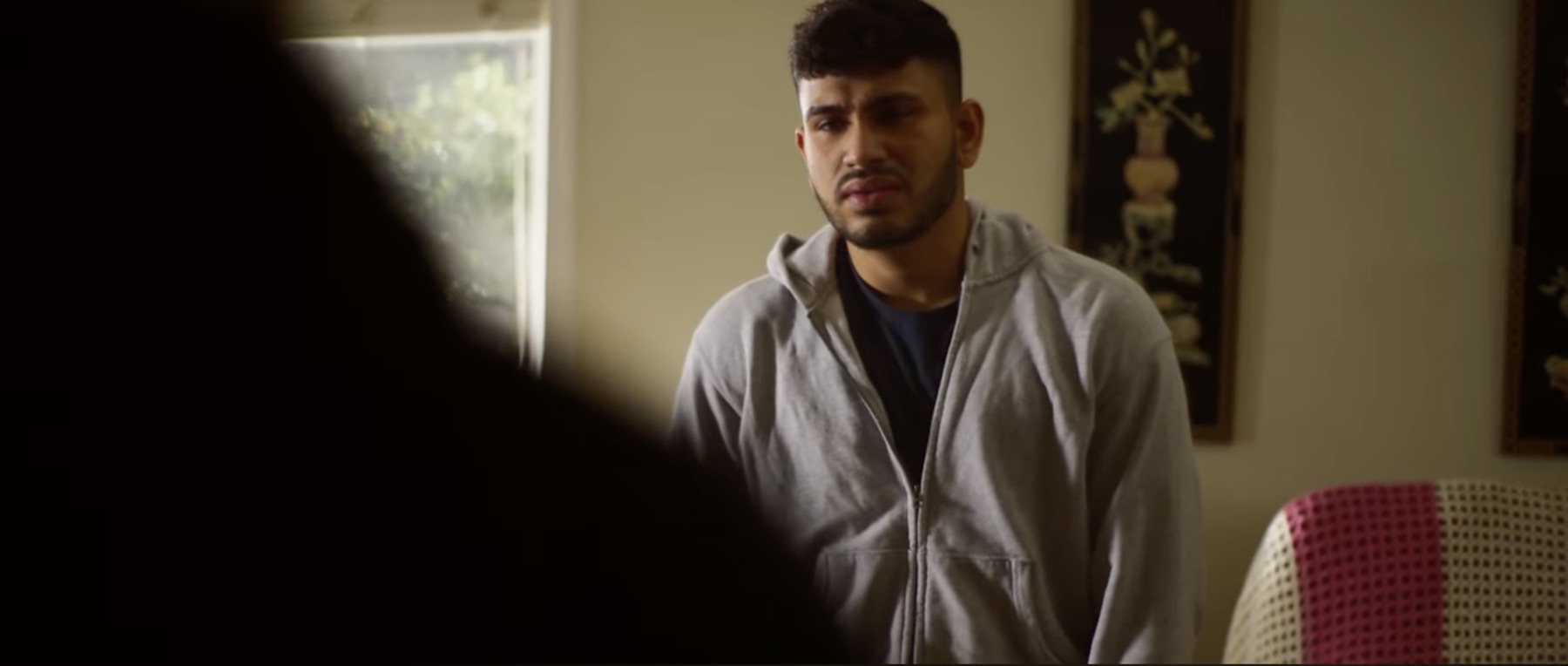 Sree as Benji in a grey hoodie, pained, looking at someone off frame