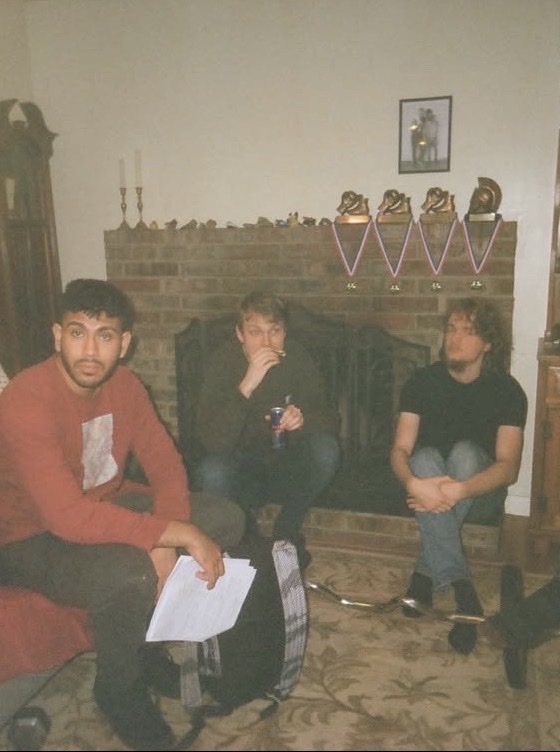 Film photo of Sree on set in a red shirt, script in hand, with cast by a fireplace